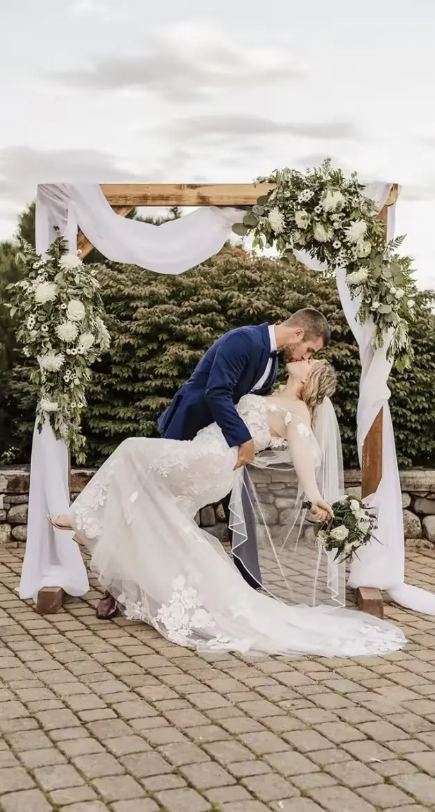 A couple kissing beneath the floral ceremony arch at Luxe Liberty